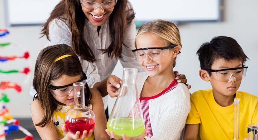 2 girls holding beakers and a boy looking down while teacher points to one of the beakers.