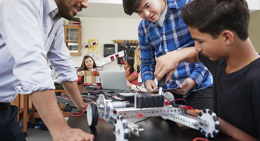Teacher with male students building robotic vehicle 