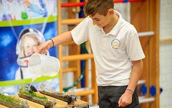 Boy pouring water into grass on a table that is being held in a cut bottle