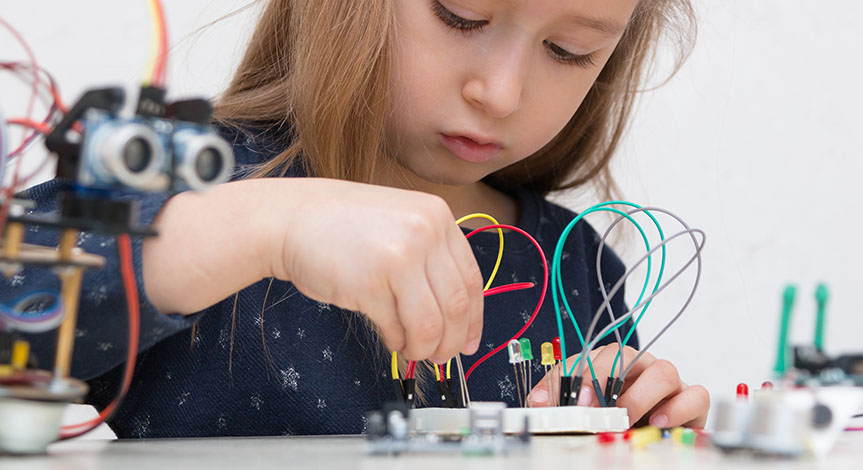 A girl constructs metal robot and program it. The boards and micro controllers are on the table.