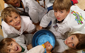 Kids looking up while mixing a big bucket of blue slime