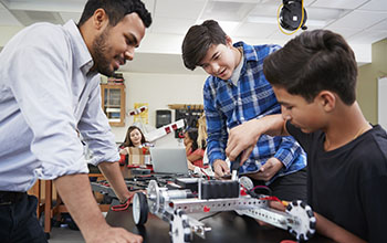Teacher with male students building robotic vehicle 