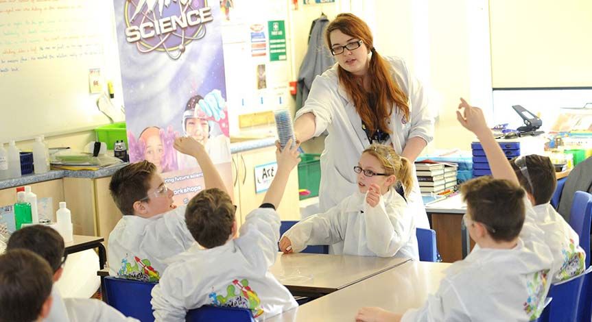 Mad Scientist passing stack of activity cups to student while kids in classroom look on
